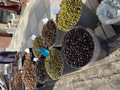       Metal buckets overflowing with green and black olives at an outdoor market stall.
  