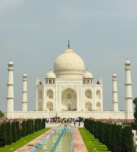      Frontal view of the white marble Taj Mahal with perfect symmetry against a pale sky.
  
