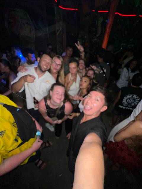       Blurry crowd of partygoers dancing and posing for a selfie in dim light.
  