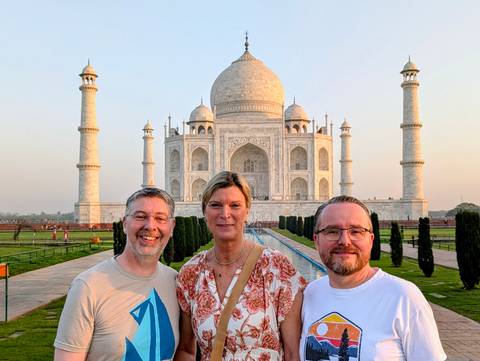       Three travellers smiling in front of the Taj Mahal in warm evening light.
  