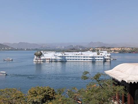      The white Lake Palace hotel floating on Lake Pichola with hazy hills behind.
  