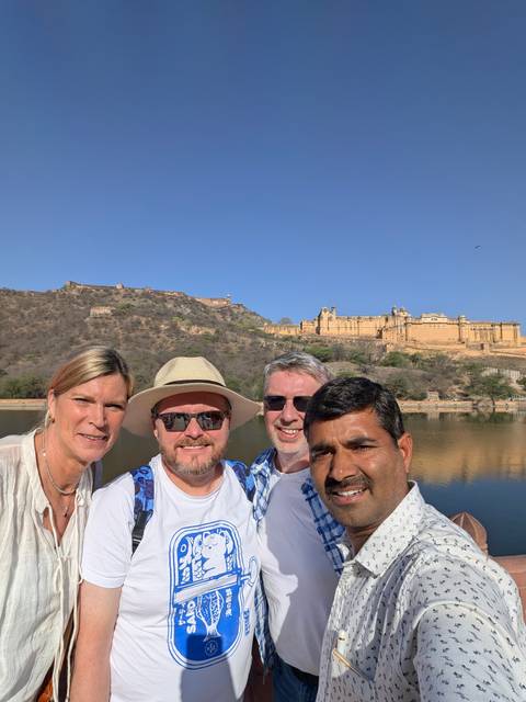       Selfie of travellers with Amber Fort and arid hills rising above a reflective lake.
  