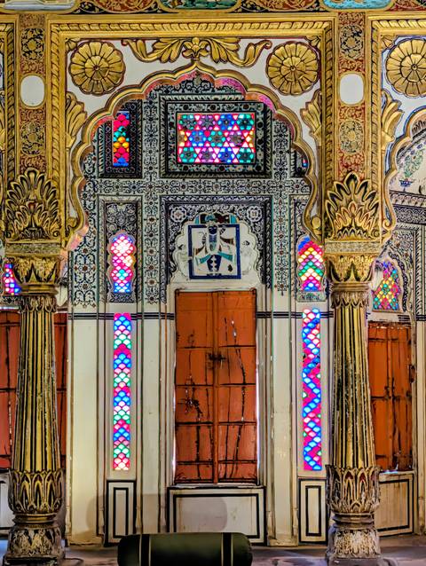       Detailed interior with ornate columns and multicoloured stained-glass panels in an Indian palace.
  
