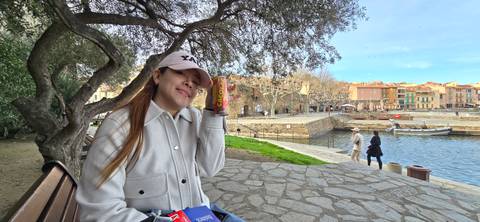       Traveler relaxing on a bench by a quaint harbor lined with pastel buildings and boats.
  