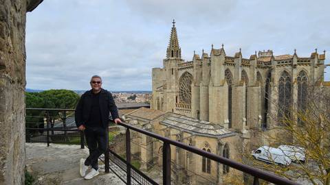       Man standing by a railing with the gothic basilica of Carcassonne rising behind him.
  