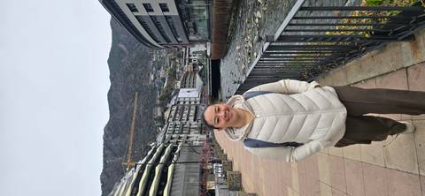       Traveler standing on a riverside promenade with modern buildings and mountains of Andorra behind.
  