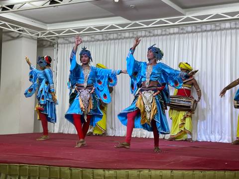       Sri Lankan dancers in vibrant blue and yellow costumes performing on an indoor stage.
  