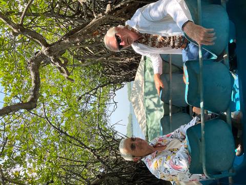       Older couple seated in a small boat gliding through dense mangrove tunnels.
  