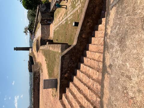       Historic coastal fort ramparts with stone steps and a distant watchtower under clear skies.
  