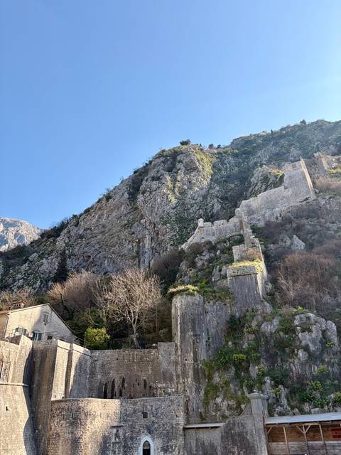       Steep limestone cliffs with ancient fortress walls climbing the mountainside above Kotor.
  