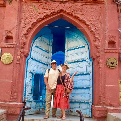       Two tourists standing at an ornate blue city gate with bright painted doors in Rajasthan.
  