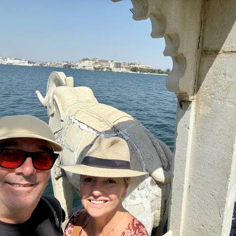       Couple’s selfie by a lakeside stone elephant sculpture with Udaipur’s city palace visible across the water.
  