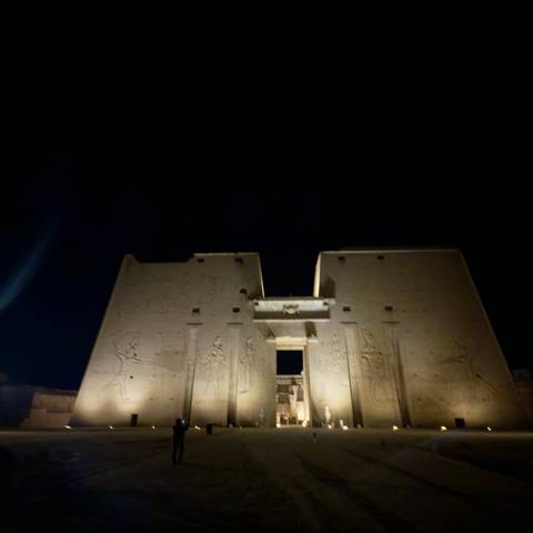       Night view of an Egyptian temple pylon illuminated against a dark sky, image slightly out of focus
  