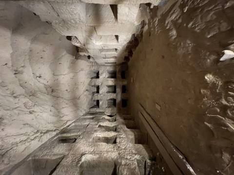       A dark, empty rock-hewn chamber with rows of small alcoves and a rough arched ceiling.
  