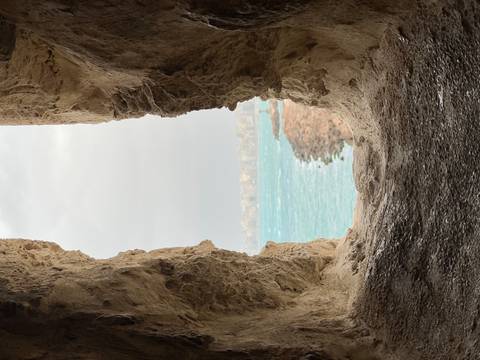       View of a windy seascape through a rough stone window opening in an ancient wall.
  