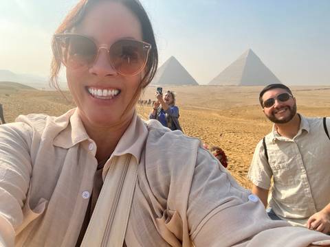       Energetic selfie with two pyramids in the hazy desert background while friends smile and photograph the scene.
  