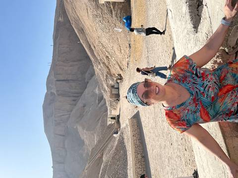       Traveller in patterned headscarf smiling in the sun-baked Valley of the Kings with steep cliffs behind.
  