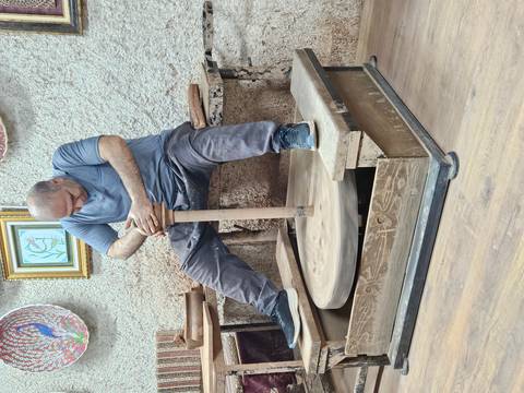       Full view of potter concentrating on shaping clay while seated at kick wheel
  