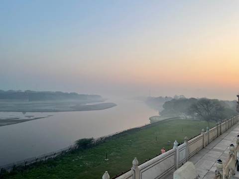       Misty sunrise over a calm river and tree-lined banks creating a tranquil pastel scene.
  