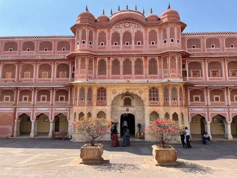       Elegant pink sandstone facade of Jaipur’s City Palace with ornamental windows and visitors in the courtyard.
  