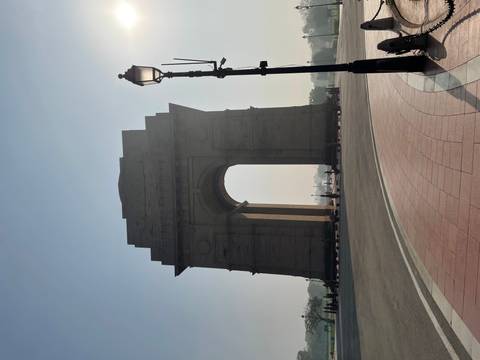       Silhouetted India Gate rises against a hazy blue morning sky on an empty boulevard in Delhi.
  