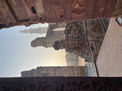       Ancient stone arch frames the towering Qutub Minar against a hazy dawn sky.
  
