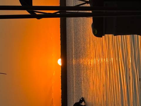       A vivid orange sun sets over calm lagoon waters, reflecting a golden path toward the viewer.
  