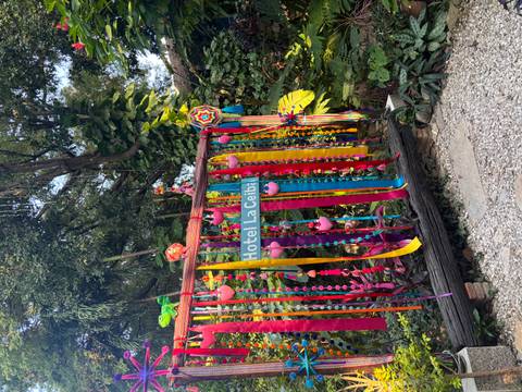       Colourful ribbon decorations and hanging ornaments frame a sign reading 'Hotel La Ceiba' amid jungle foliage.
  