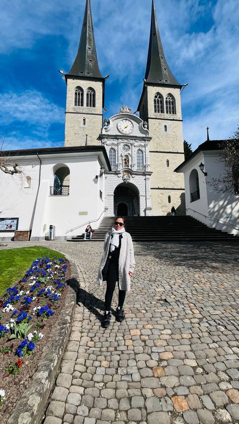       Visitor posing in front of a white church facade with grand staircase and small flower bed
  
