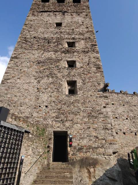       Close-up of a rough stone castle wall and tower against blue sky
  