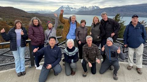       Happy tour group posing on terrace overlooking Torres del Paine peaks and lake
  