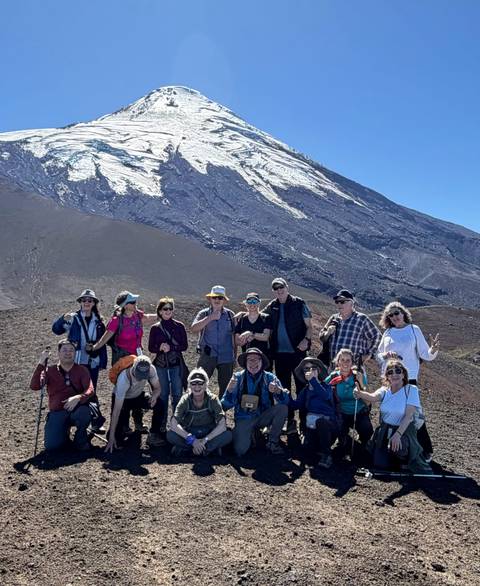       Tour group posing on volcanic plateau with snow-capped peak behind
  