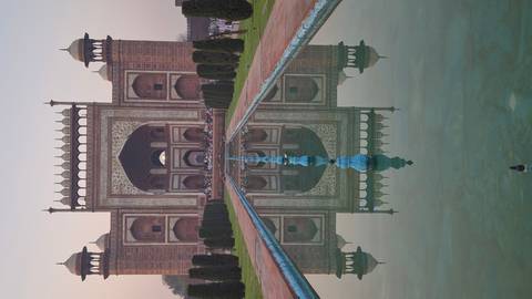       Grand sandstone gateway to the Taj Mahal complex mirrored perfectly in the long reflecting pool at dawn.
  