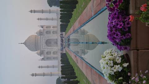       Iconic marble Taj Mahal framed by reflecting pool and flower beds in soft dawn light.
  