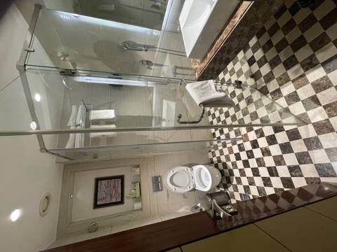       Spacious hotel bathroom with checkered floor, glass shower enclosure and wall-mounted toilet.
  