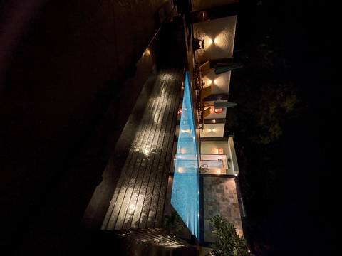       Illuminated outdoor swimming pool at night with loungers and ambient lighting reflecting on the water.
  