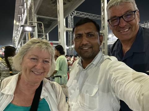       Selfie of smiling tourists and local guide on a busy railway platform at night.
  