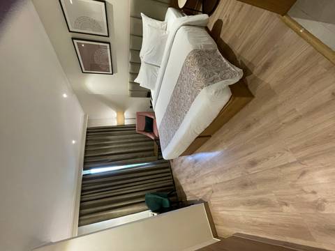       Bright hotel room with wood flooring, large window and neatly dressed double bed.
  