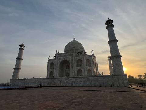       Side silhouette of the Taj Mahal at dawn with soft sun emerging behind a minaret.
  