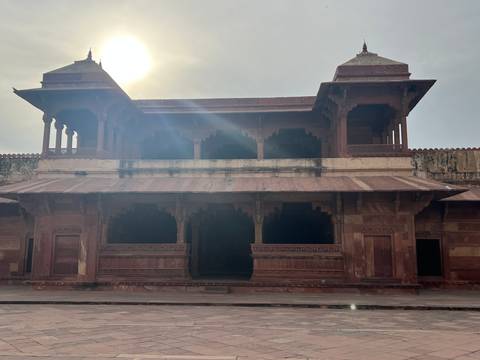       Backlit red sandstone pavilion in Fatehpur Sikri with sun glare creating dramatic rays.
  