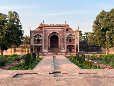       Symmetrical Mughal garden leading to an ornate red and white gateway set amid manicured flowerbeds.
  