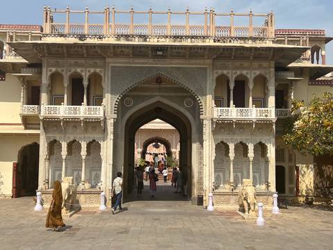       Decorative arched entrance of a palace courtyard with visitors walking through elaborately carved stonework.
  