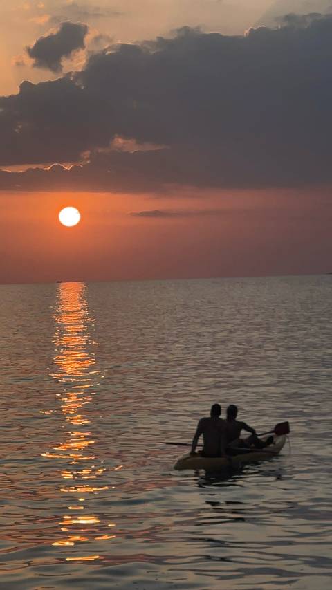      Orange sun low on the horizon casting a bright reflection over gentle sea ripples.
  