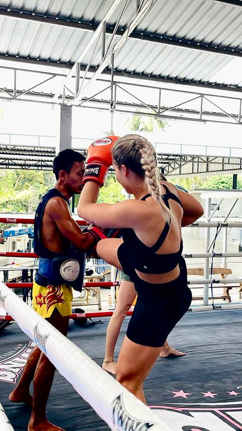       Close-up of Muay Thai sparring with a female fighter driving a knee into a trainer’s pads.
  