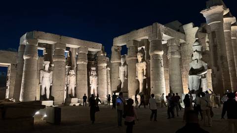       Night illumination of towering columns and statues inside Luxor Temple with tourists walking through
  