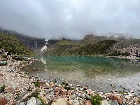       Emerald-green alpine lake beneath steep, cloud-shrouded peaks with small groups of visitors along the shore.
  