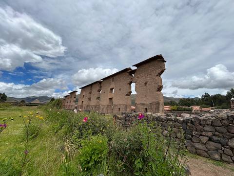       Long adobe and stone Inca ruin walls rising beside a meadow dotted with wildflowers.
  