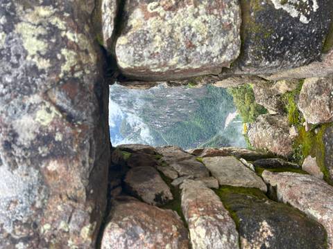       Stone window opening with moss framing a lush gorge and misty cliffs below.
  