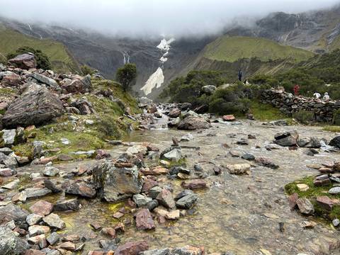       Mountain stream flowing over colorful rocks beneath glacier-clad cliffs.
  