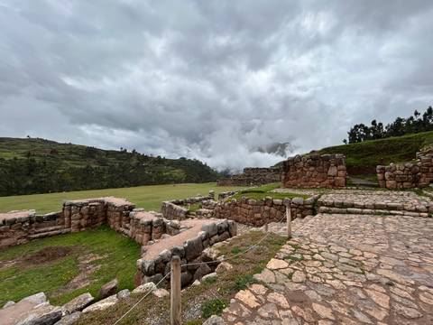       Stone terraces and pathways of a high-altitude Inca site set against misty hills.
  